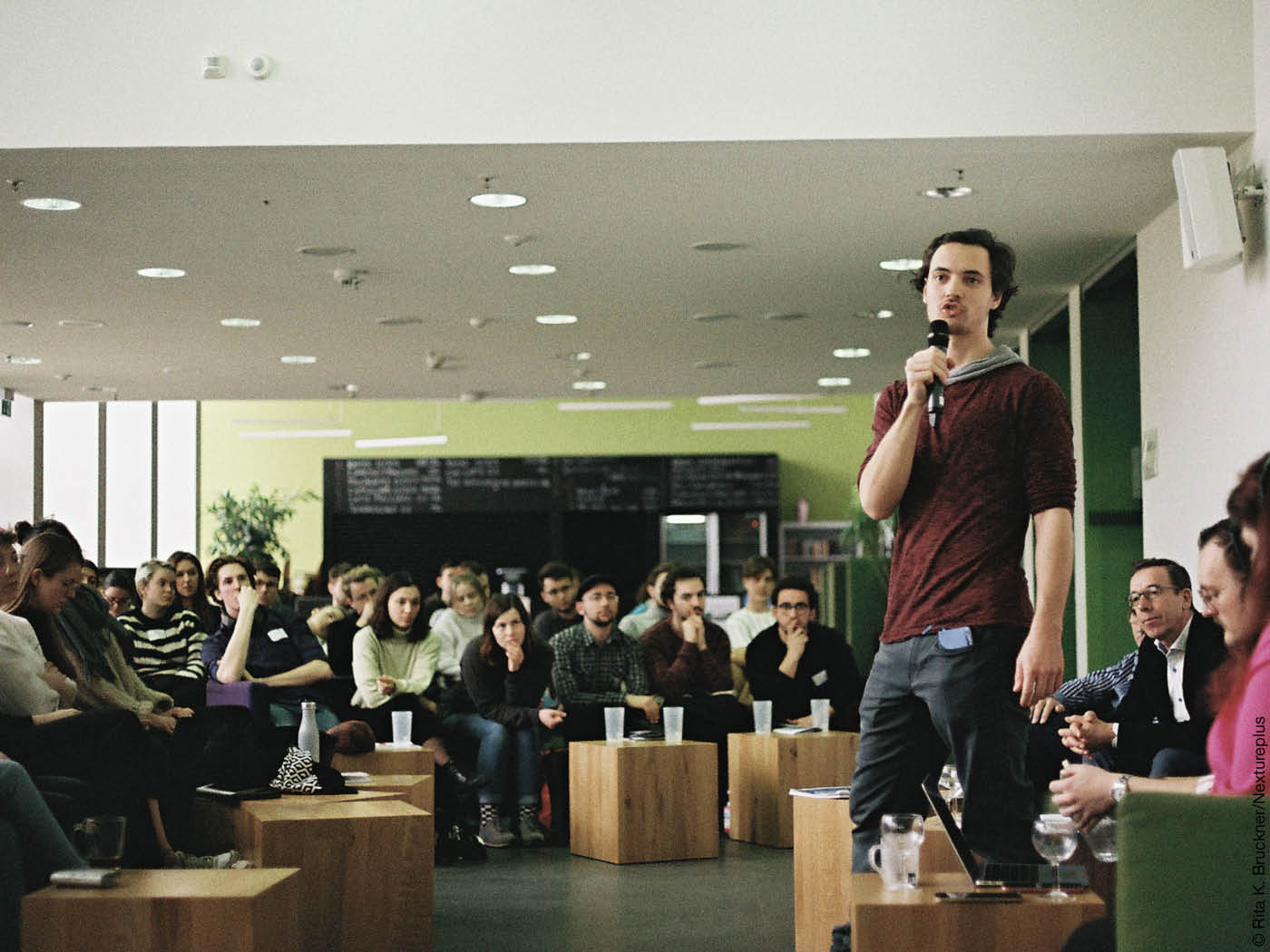 Ein junger Mann spricht vor Publikum ins Mokrofon.