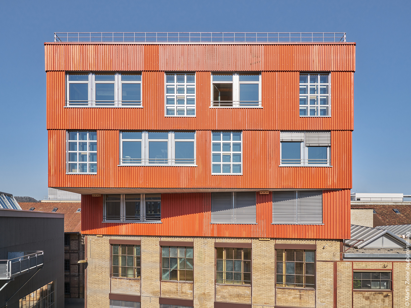 Gebäudeaufstockung mit orangener Fassade und großen Fenstern