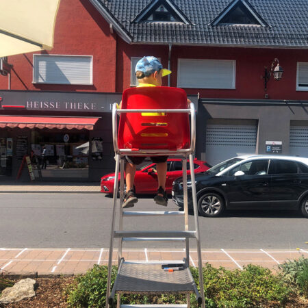 Kind sitzt am Straßenrand auf einem Hochsitz