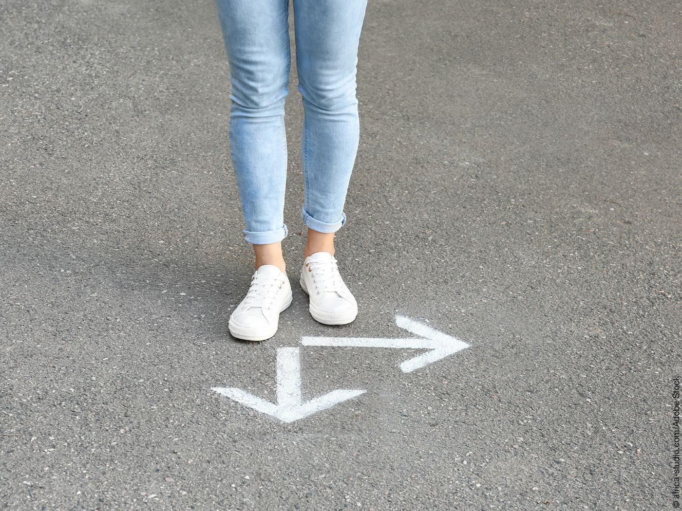 Zwei Frauenbeine vor zwei Pfeilen auf dem Asphalt, einer zeigt geradeaus, einer zur Seite.