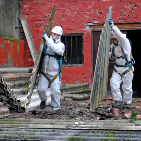 Zwei Personen in Schutzanzügen entsorgen alte Asbestplatten