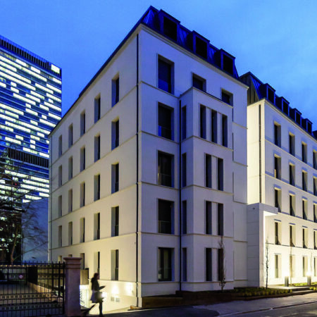Mehrfamilienhaus am Abend mit Hochhaus im Hintergrund