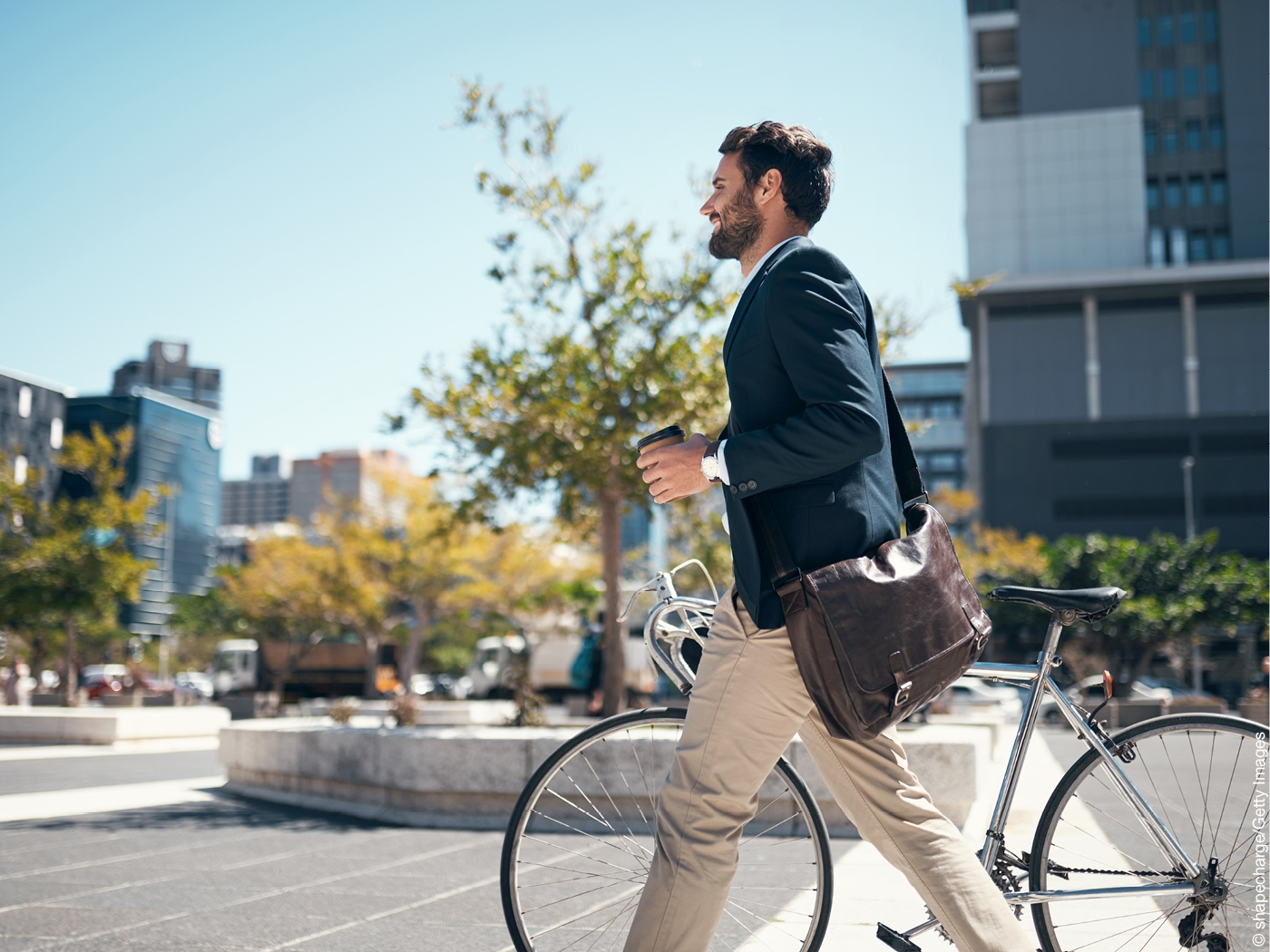 Mann mit Kaffeebecher, der ein Fahrrad durch die Stadt schiebt