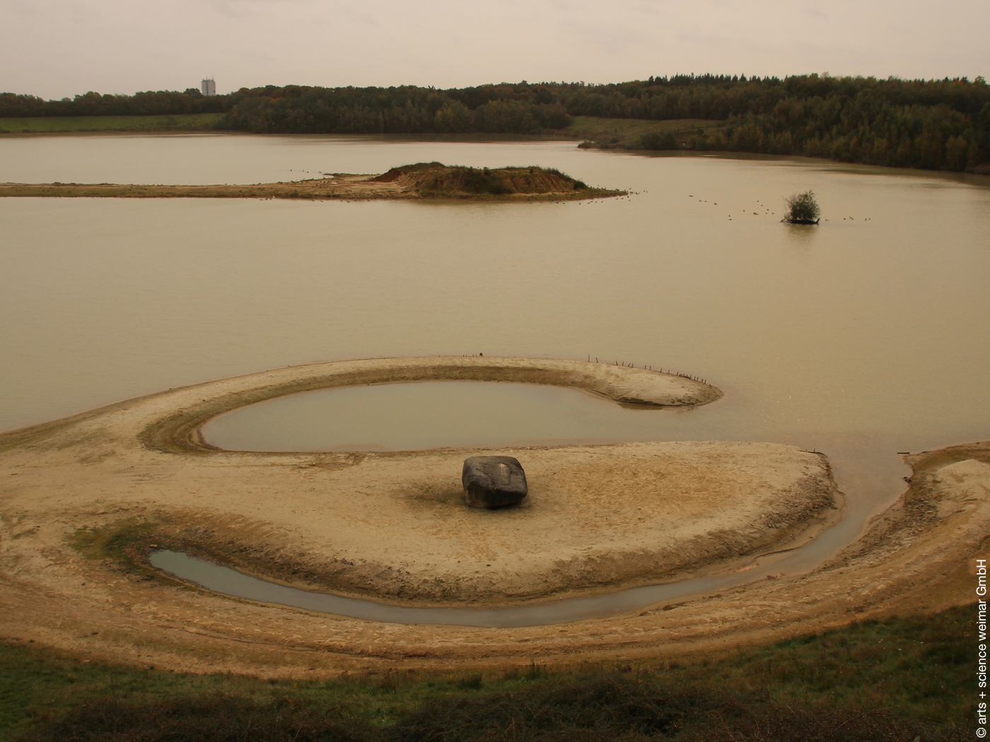 Baggersee mit spiralförmiger Sandbank und Felsen