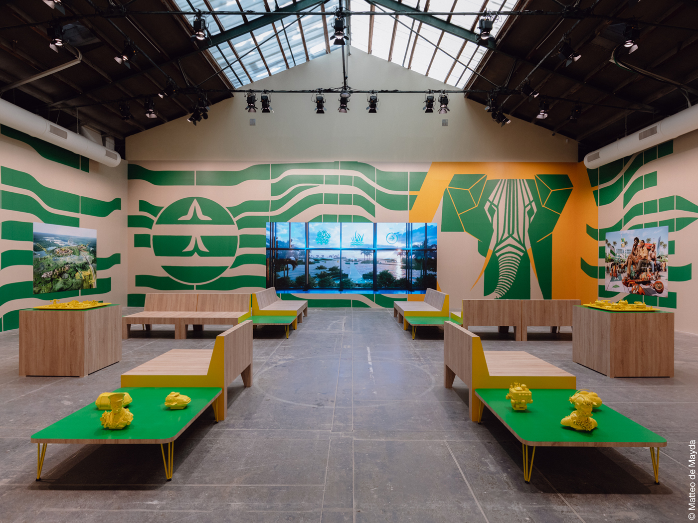 Das Bild zeigt den Nachbau einer grün-gelben Flughafenlounge mit afrikanischen Motiven an den Wänden, Tischen und Sitzbänken.