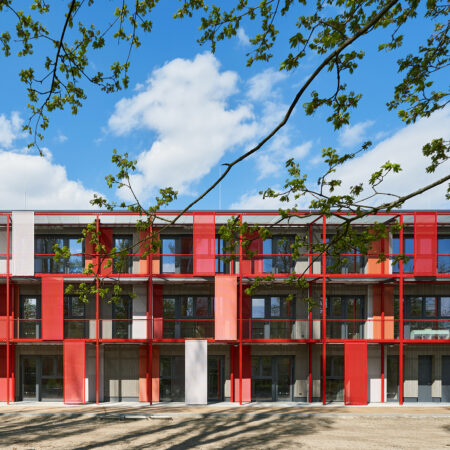Rotes Gebäude mit vielen Fenstern, Balkonen und Sonnenschutzelementen