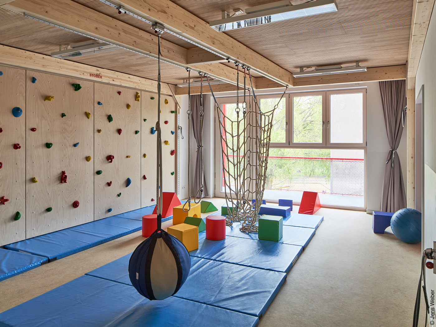 Ein Raum mit Spiel- und Sportgeräten, überdimensionalen Bauklötzen, einer Kletterwand und blauen Bodenmatten