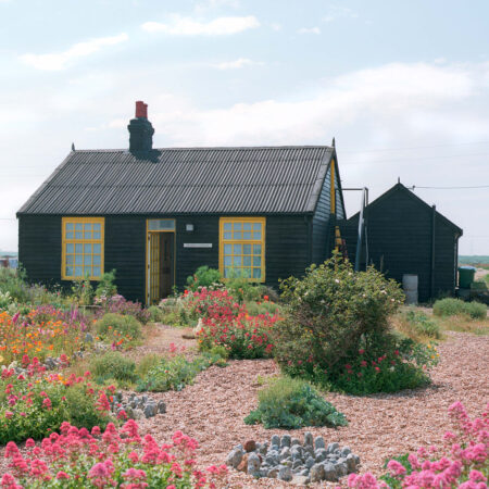 Schwarze Holzhütte in Garten mit Kiesflächen und bunten Blumen