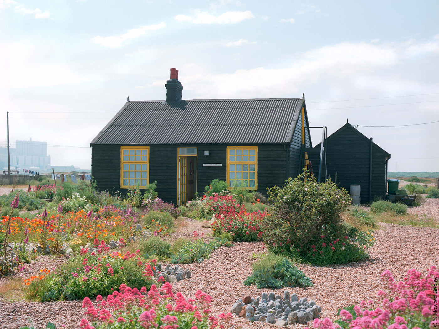 Schwarze Holzhütte in Garten mit Kiesflächen und bunten Blumen
