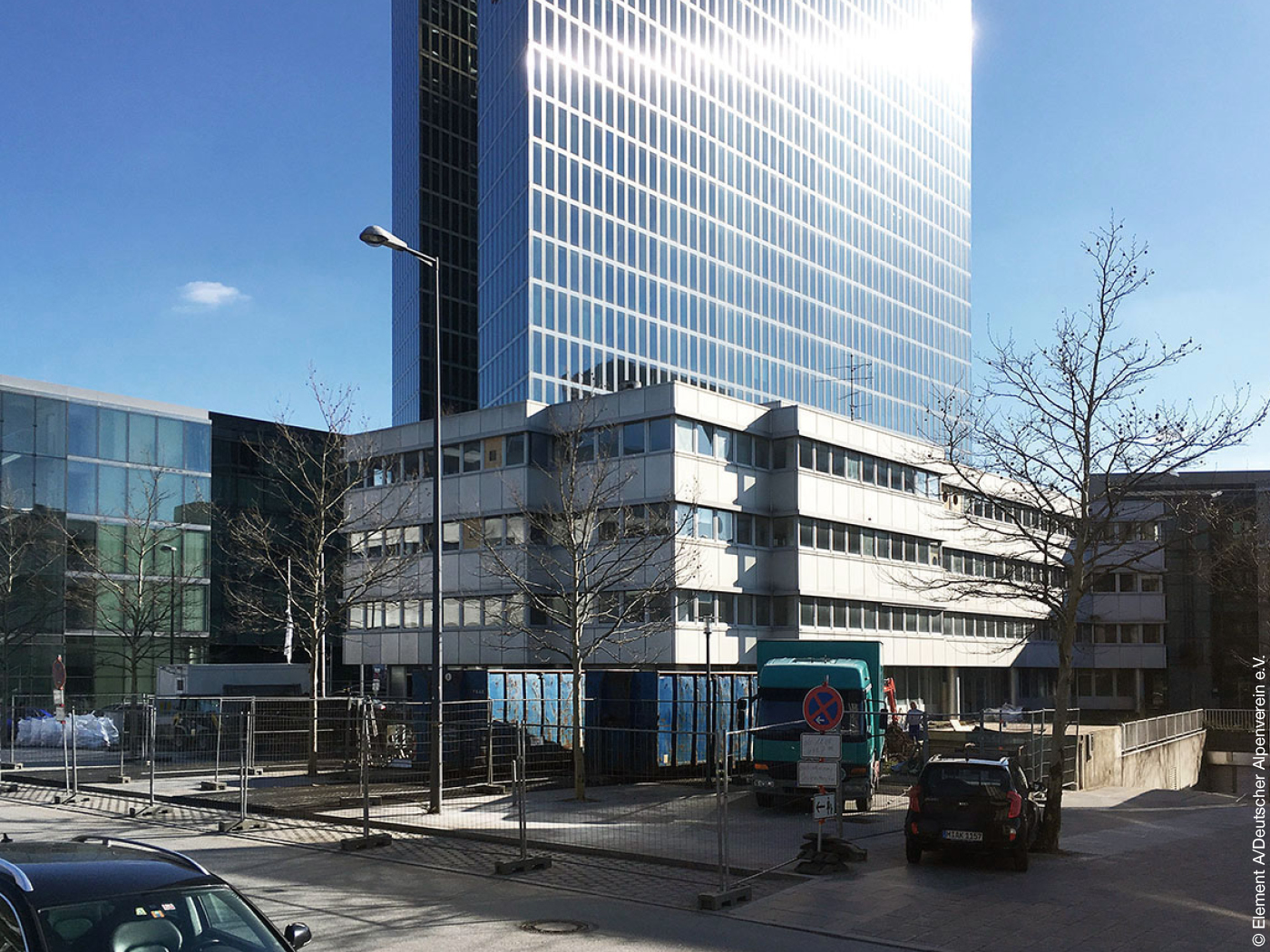 Niedriges Bürohaus vor Hochhaus mit vielen Fenstern, deren Scheiben in der Sonne blitzen