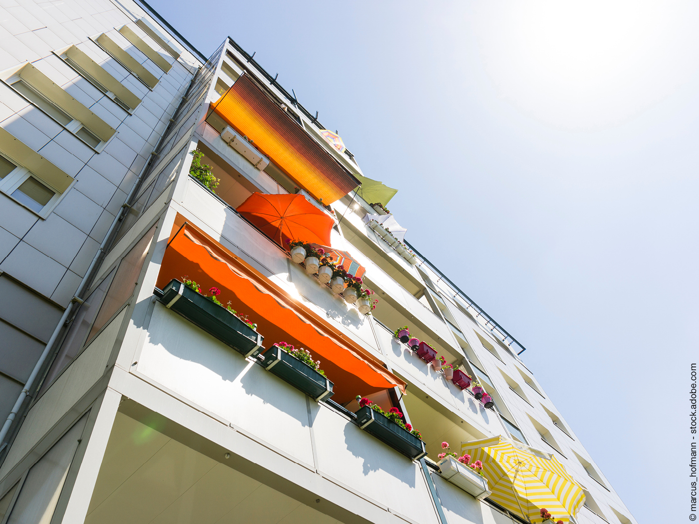 Hochhausfassade mit Sonnenschirmen und Blumen auf den Balkons