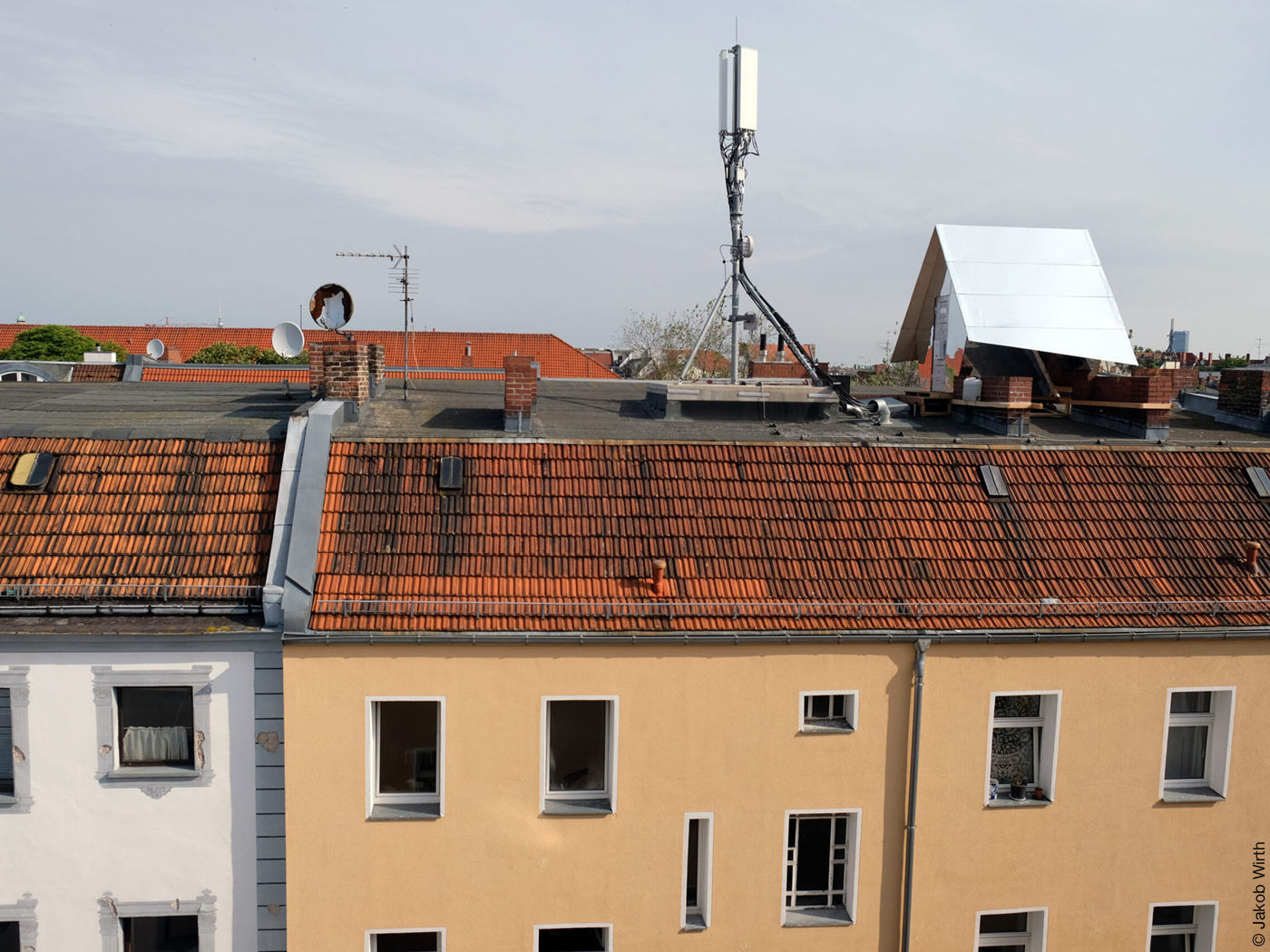 Verspiegeltes Tiny House auf einem Hausdach neben Mobilfunkantenne