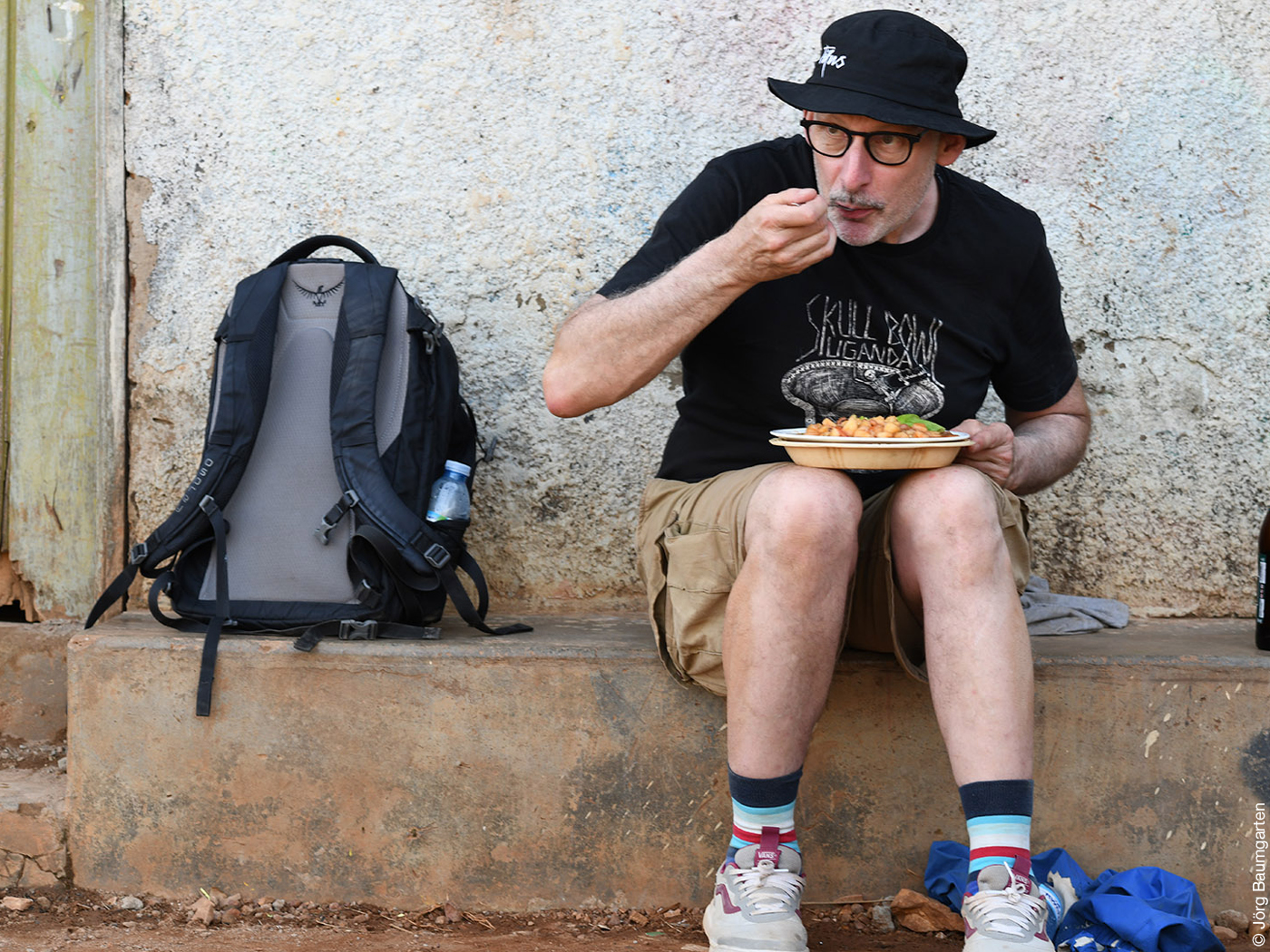 Das Foto zeigt Ralf Maier, der auf einem Vorsprung vor einer Hauswand sitzt und aus einem Teller isst.