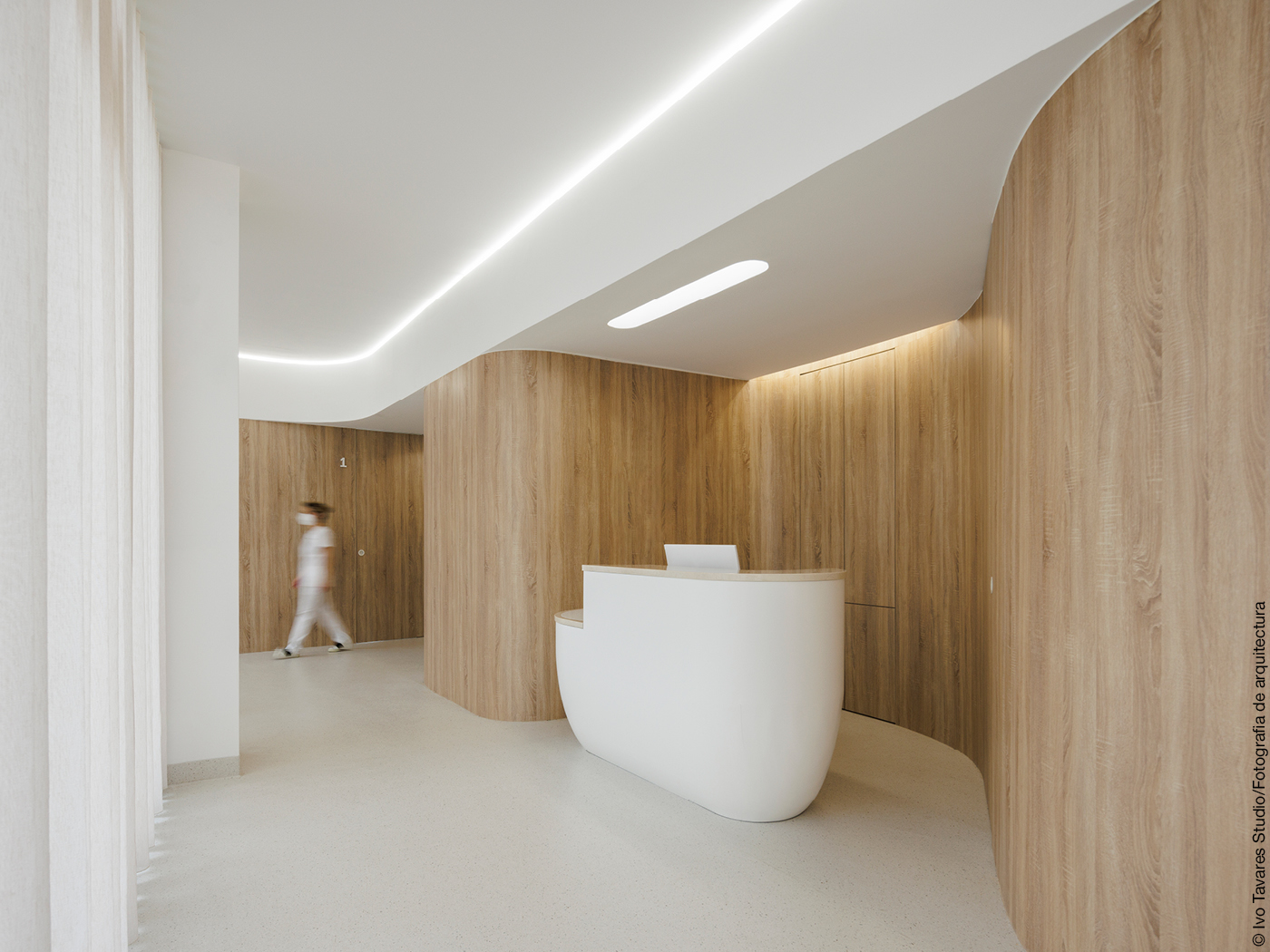 Eingangsbereich einer Zahnklinik mit Holzwänden und weißen Möbeln und weißem Boden.