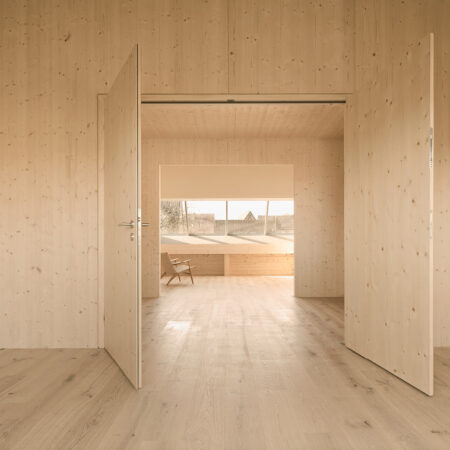 Mehrere, miteinander verbundene Räume unter dem Dach mit Holzverkleidung und Holzfußboden, durch deren geöffnete Türen man zu einem weiteren Raum mit einer einer großen Fensterfront in der Dachschräge schauen kann.