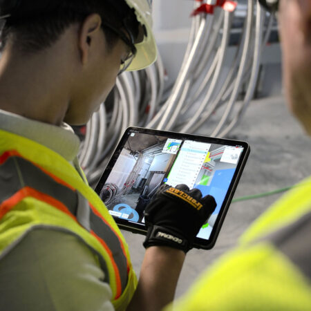 Zwei Baustellen-Arbeiter schauen auf den Bildschirm eines Tablets und begutachten die virtuelle Version ihrer Baustelle.