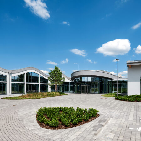 Bürogebäude in Paderborn mit geschwungenen Dächern und großen Fensterfronten, davor einen asphaltierten Platz mit bepflanzten Beeten