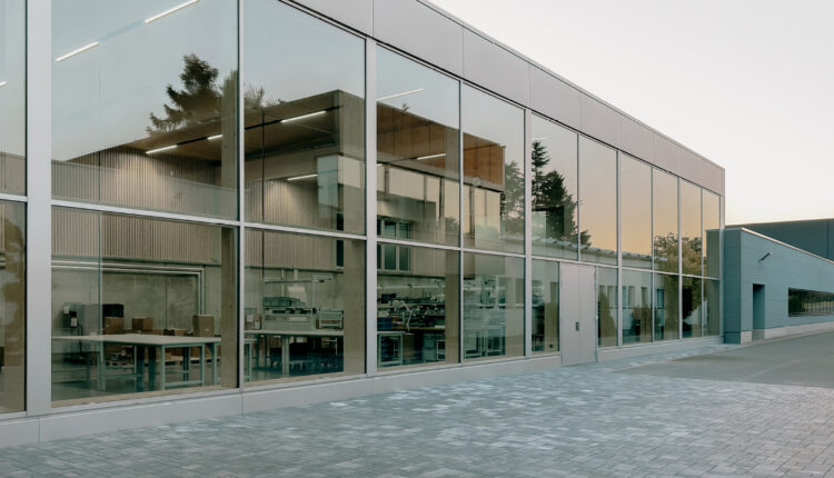 Glasfront der Werkshalle einer Fabrik, in deren Fenstern sich die untergehende Sonne spiegelt.