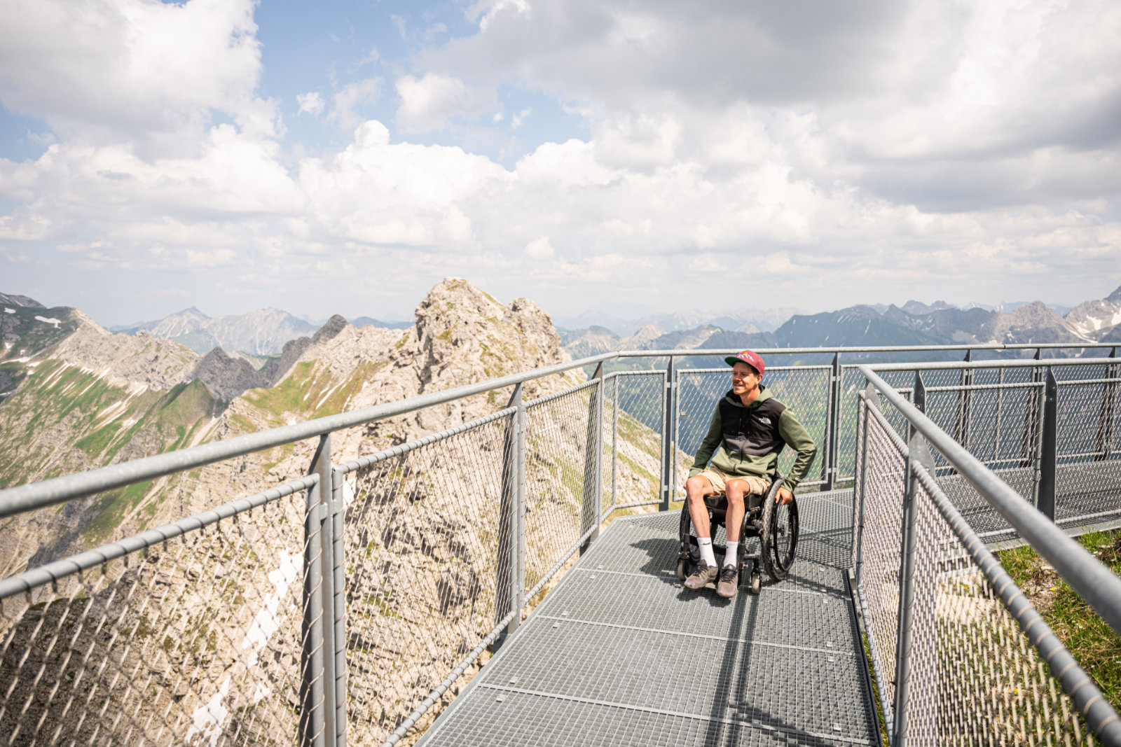 Rollstuhlfahrer auf einem Metallsteg mit Aussicht auf Berge
