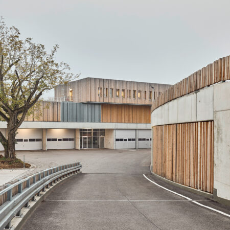 Menschenleer Auffahrt zu einem Betriebshof mit beigebraun-roströtlicher Fassade.