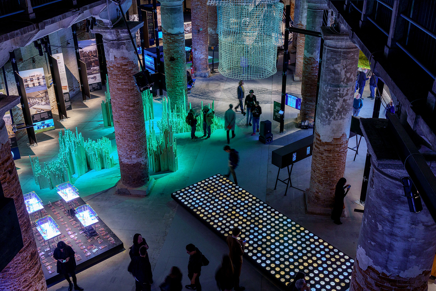 Menschen wandeln durch einen Ausstellungsraum, der in Blau, Grün und Türkis getaucht ist.