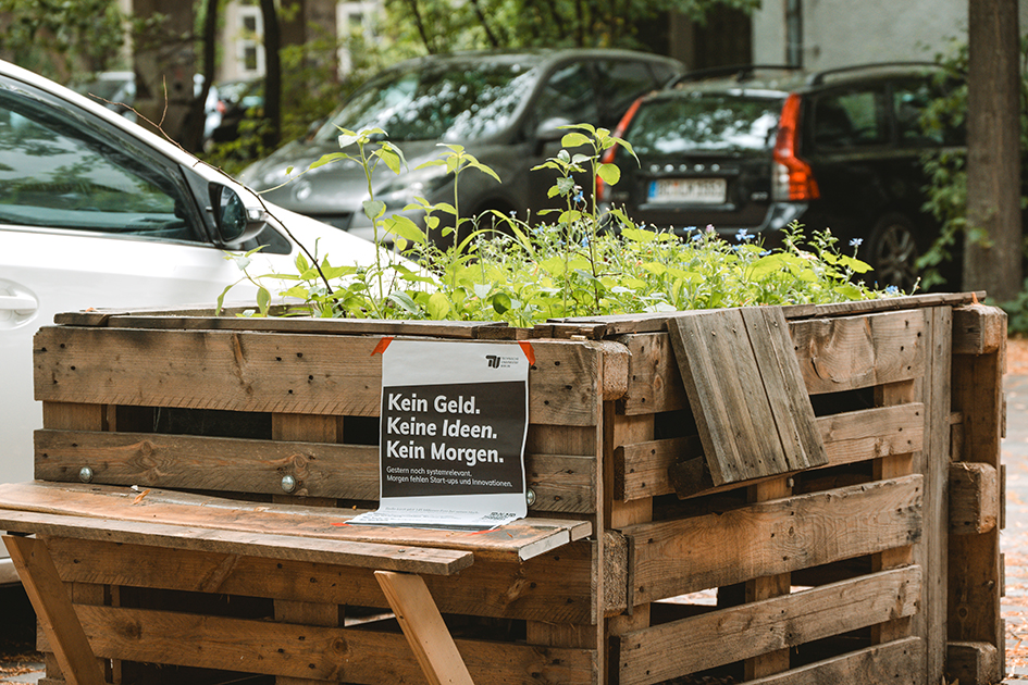 Ein selbsgebautes Hochbeet mit Pflanzen, an dem ein Protestplakat hängt.