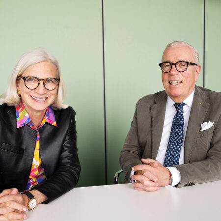 Zu sehen ist Andrea Gebhard, Landschaftsarchitektin und Stadtplanerin, seit 2021 Präsidentin der BAK. Zu sehen ist ebenfalls Klaus Reinhardt, Facharzt für Allgemeinmedizin, seit 2019 Präsident der Bundesärztekammer. Beide sitzen mit gefalteten Händen an einem mattweißem Tisch vor einer lindgrünen Wand.
