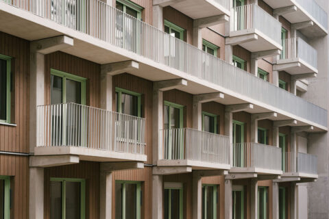 Wohngebäude mit Holzfassade, quadratischen Fenstern mit grünen Fensterrahmen und weißen Balkons